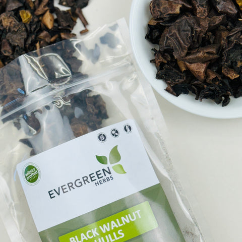 Evergreen Herbs Black Walnut Hulls in a clear resealable pouch with dried hull pieces displayed beside it in a white bowl.