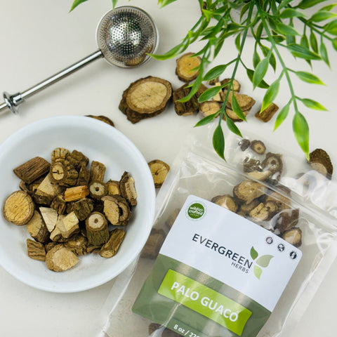 Evergreen Herbs Palo Guaco dried cut roots displayed in a white bowl and a branded pouch, with a tea infuser and green leaves on a clean white surface.