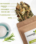 Evergreen Herbs Adelgazar loose-leaf tea spilling from a kraft pouch with labeled ingredients and a teacup beside it.