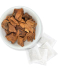 A bowl filled with Cocolmeca bark pieces alongside tea bags on a white background.