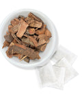White bowl of dried cuachalalate bark with individual herbal tea bags arranged beside it on a clean white background.