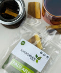 Evergreen Herbs Palo Azul wood pieces in a clear resealable pouch with a tea infuser and brewed tea beside it.