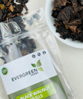 Evergreen Herbs Black Walnut Hulls in a clear resealable pouch with dried hull pieces displayed beside it in a white bowl.