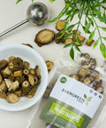 Evergreen Herbs Palo Guaco dried cut roots displayed in a white bowl and a branded pouch, with a tea infuser and green leaves on a clean white surface.