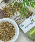 Evergreen Herbs Burdock Root in a bowl and a resealable pouch, with loose burdock pieces and a tea infuser displayed on a table.