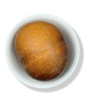 A single Guaje Cirial with a beige-brown skin placed inside a white bowl on a white background.
