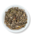 A white bowl filled with dried loose leaf tea mix, with visible herbs such as artichoke and dandelion root.