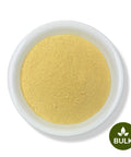 A white bowl filled with yellow Quassia powder on a white background, with a 'BULK' label in the lower right corner.