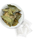 A bowl filled with soursop leaves and several individual tea bags spread out in front of it, suggesting the product is Soursop Tea Bags.