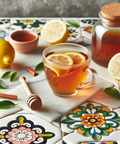 Hot tea with lemon slices in a glass cup surrounded by fresh lemons, honey, cinnamon sticks, and leafy herbs on colorful tile.