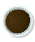 A bowl of black walnut hull powder on a white background.