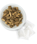 A bowl filled with dried Palo Guaco leaves next to several tea bags on a white background.