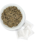 A white bowl filled with raspberry leaf powder, next to individual white tea bags.