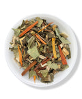 A bowl of dried herbal tea leaves and pieces, including green leaves and brown stems, indicative of the product 'Nervios Te (Relax Tea)'.