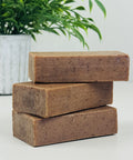 Three stacked bars of brown soap with a plant in the background