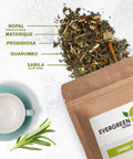 Herbal tea blend spilled beside a kraft paper Evergreen Herbs pouch labeled Diabe-Te, with ingredients including nopal, matarique, prodigiosa, guarumbo, and sábila, displayed with a teacup on a white textured background.