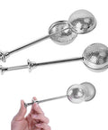 Three stainless steel tea infuser sticks with perforated ball strainers, including one shown held by hand.