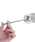 A hand holding a stainless steel tea infuser with a perforated ball design.